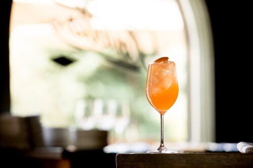 A cocktail in a wine glass with an orange garnish.