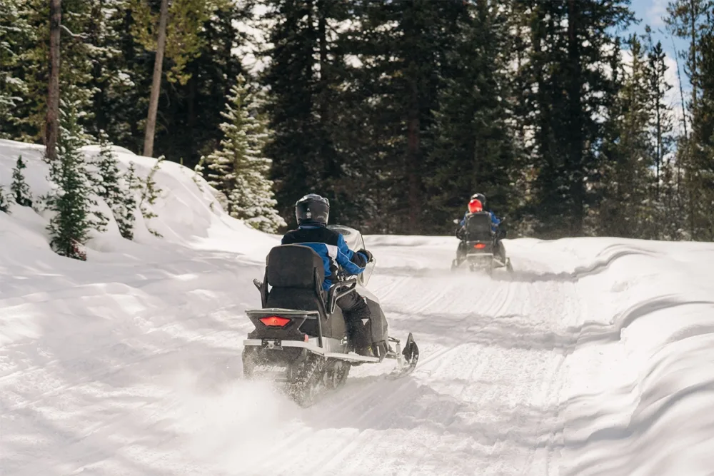 Two people snowmobiling in the mountains.