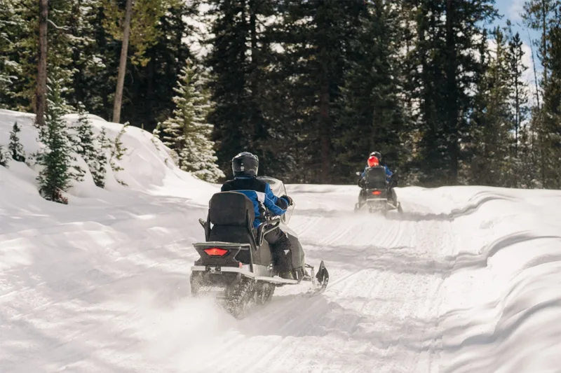 Two people snowmobiling in the mountains.