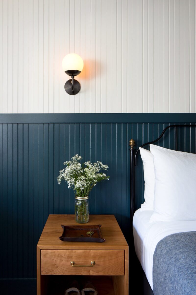 A guest bed and nightstand with flowers at Anvil Hotel in Jackson.